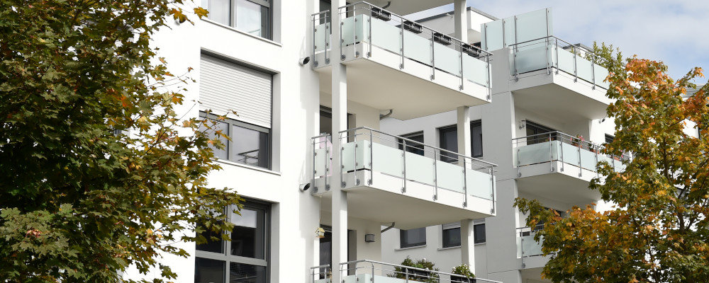 Ausschnitt eines Mehrfamilienhauses mit Balkonen. Links und rechts ragen Äste ins Bild