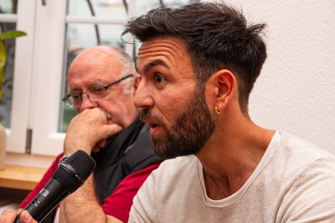 Takis Mehmet Ali mit Mikrophon und stark gerunzelter Stirn. 